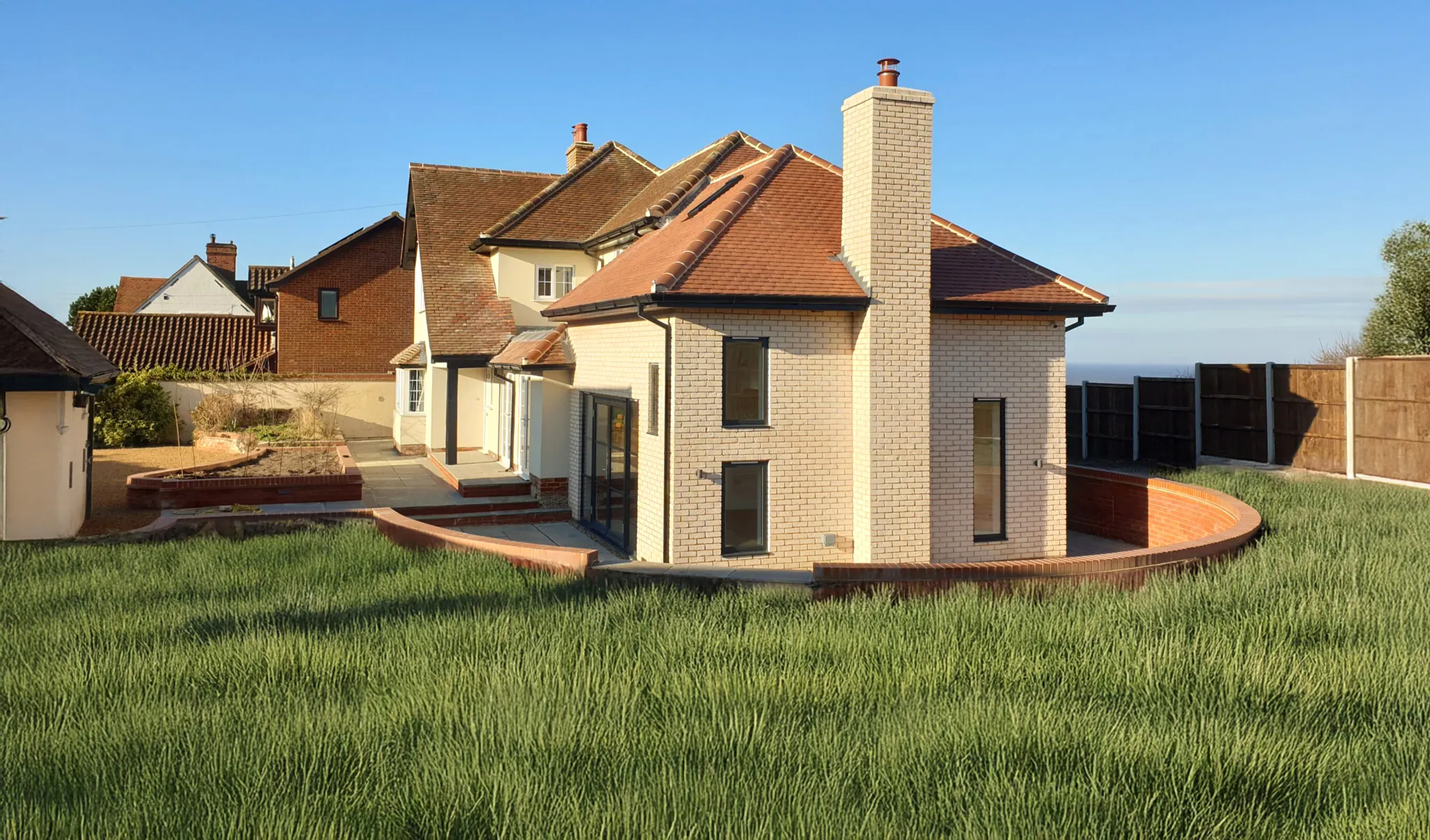 Newly built traditional brick house with red tiled roof, double-glazed windows, front garden and countryside view under clear blue sky