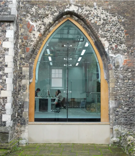 Old arched window with modern glass showing an office inside with people sitting at a desk