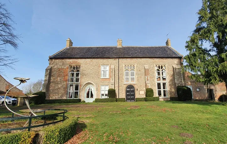 Exterior shot of an old country home with ornate windows and a scupture in the garden
